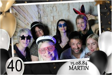 Gäste mit Fotobox-Requisiten feiern Martins 40. Geburtstag.