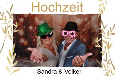 Sandra & Volker bei ihrer Hochzeit, lachend und verkleidet mit grünen und pinken Hüten, in einem Fotobox-Bild